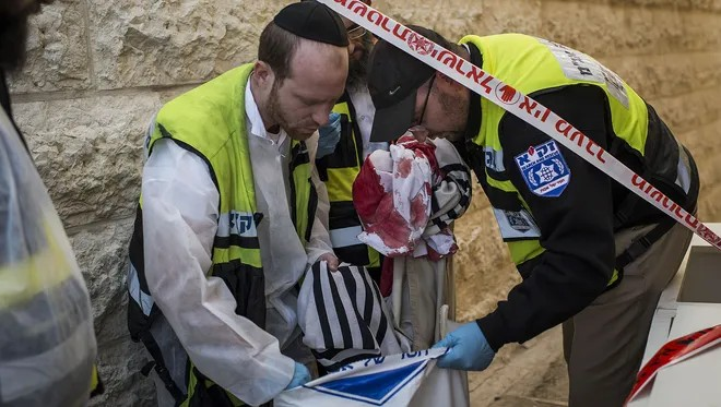 Emergency personnel holding a bloody prayer shawl